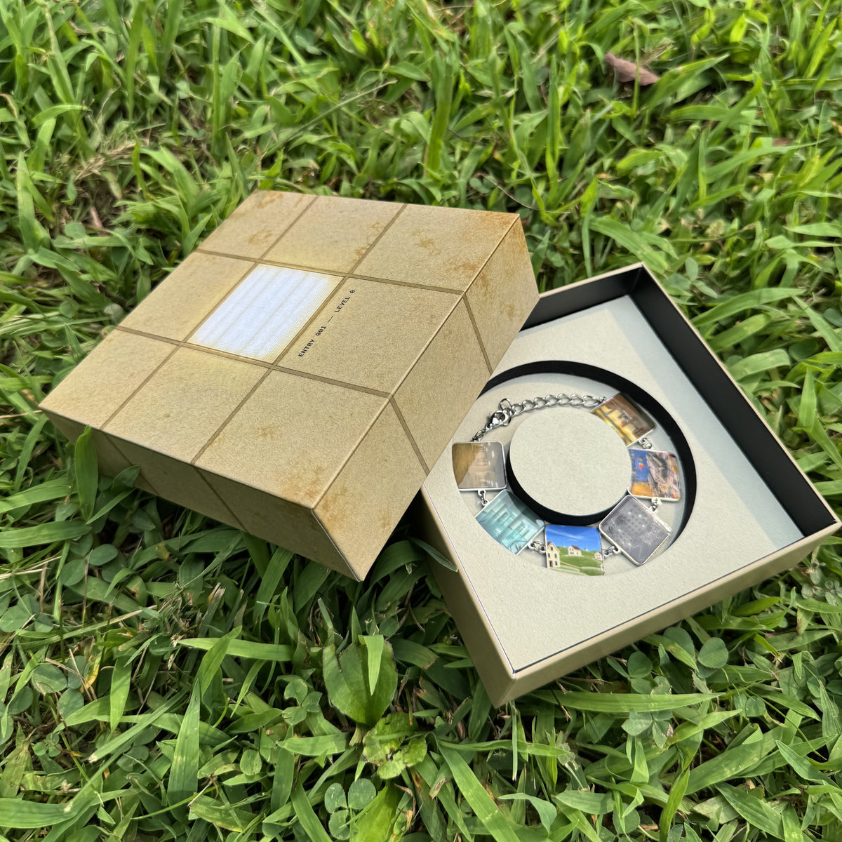 Entry 001 collector box, aged ceiling tile exterior with AIA logo panel, bracelet charms alongside