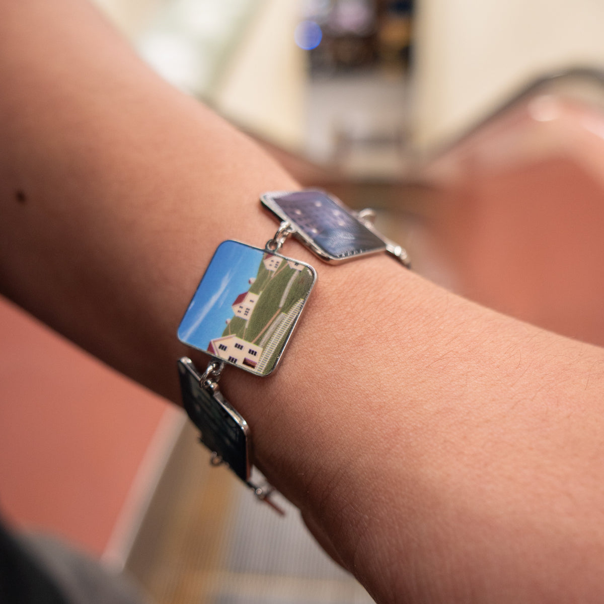 Backrooms Bracelet on wrist, Level 94 charm showing houses on a green hill under blue sky, UV-printed stainless steel